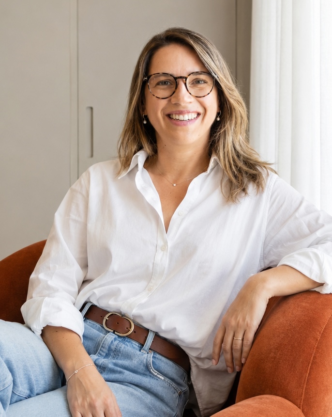 Carolina Justo sentada e sorrindo, com camisa branca